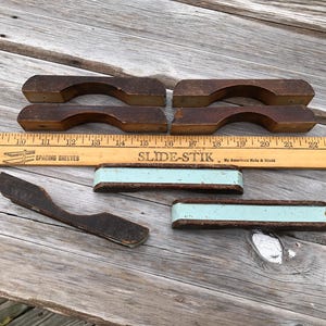 May include: Four wooden handles with a rounded top and a flat bottom. Two of the handles have a light blue painted stripe. The handles are on a wooden surface with a ruler that reads "SLIDE-STIK".
