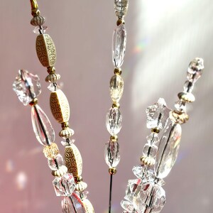 May include: Three decorative metal rods adorned with a vertical arrangement of clear faceted glass beads, textured cream-coloured oval beads, and small gold-toned spacers. The beads are strung along thin metal stems, creating a light-catching display.