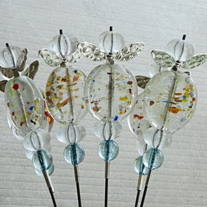 May include: Five glass baubles with silver accents and colourful flecks. Each bauble is suspended from a silver wire and has a blue glass bead at the bottom.
