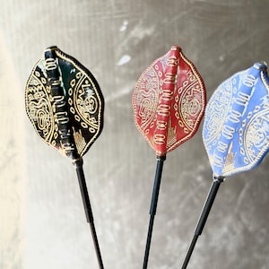 May include: Three decorative leaf-shaped objects with intricate gold designs. One is black, one is red, and one is blue. Each is mounted on a black stem, creating a unique and artistic display.