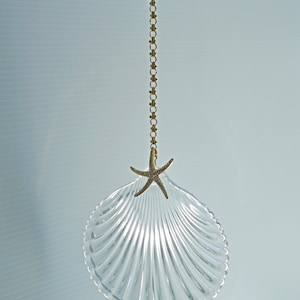 May include: A clear glass seashell ornament with a gold chain and a gold starfish with rhinestones hanging from it.