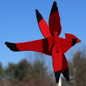 May include: Red cardinal wind spinner with black accents. The cardinal is in flight with its wings spread out. The wind spinner is made of wood and is painted red and black.