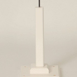 May include: A white wooden display stand with a square base and a tall, rectangular post. A thin, dark metal rod extends from the top of the post. The stand is designed to hold an item for display.