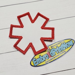 Op de afbeelding: Rode geborduurde ster-patch met een wit centrum. De patch is op een witte houten achtergrond.