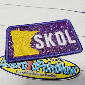May include: Purple and yellow iron-on patch with the outline of the state of Minnesota and the word "SKOL" in white lettering.
