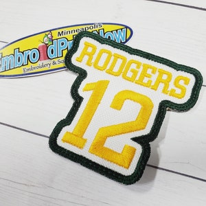 May include: Green and white embroidered patch with the name "RODGERS" and the number "12" in yellow thread.