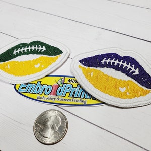 May include: Two embroidered iron-on patches shaped like lips with a football design. The top patch is green and yellow, and the bottom patch is purple and yellow.