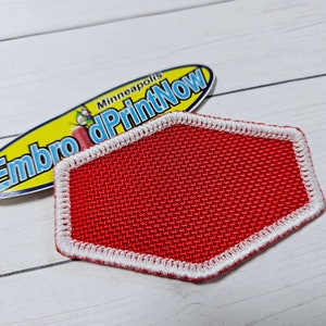 May include: Red hexagonal patch with a white border. The patch is made of a woven fabric with a textured surface.