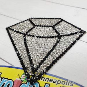 May include: A black and silver diamond-shaped rhinestone iron-on patch. The patch is made of small rhinestones in a diamond shape.