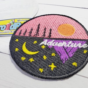 May include: Embroidered patch with a pink sunset, purple mountains, a yellow moon, and stars on a black background. The text "Adventure" is written in white on the mountains.