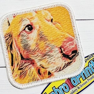 May include: Close-up of a white, embroidered patch with a colorful image of a dog's face. The dog has brown eyes, a pink nose, and a yellow and orange coat.