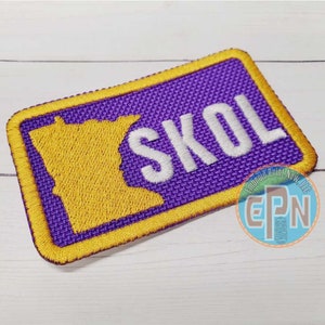 May include: Purple and yellow embroidered patch with the outline of the state of Minnesota and the word "SKOL" in white.