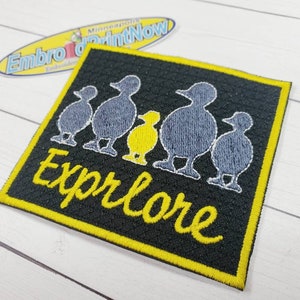 May include: Black iron-on patch with a yellow border. The patch features a group of five gray and yellow stylized ducks with the word "Explore" in yellow cursive lettering.
