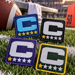 May include: Four square embroidered patches featuring a large letter C and five stars. One patch is blue with a light blue C and yellow stars. The others are black, purple, and green, each with a white C and one yellow star among four white stars.