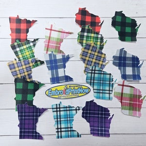 May include: A collection of fabric cutouts in the shapes of the states of Minnesota and Wisconsin. The cutouts feature various plaid patterns in colors like red, green, blue, and purple. The logo "Embro dPrintNow" is visible.