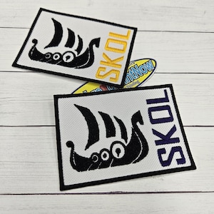 May include: Two rectangular patches with a black Viking ship design and the word "SKOL" in yellow and purple. The patches are on a white background with a black border. The patches are likely for clothing or accessories.