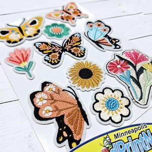 May include: A sheet of iron-on patches featuring colorful butterflies, flowers, and a sunflower. The patches are perfect for adding a touch of whimsy to clothing, bags, or other fabric items.