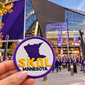 May include: A circular embroidered patch with a white background and a purple border. It features a purple silhouette of the state of Minnesota above the yellow embroidered text SKOL and the black embroidered text MINNESOTA.