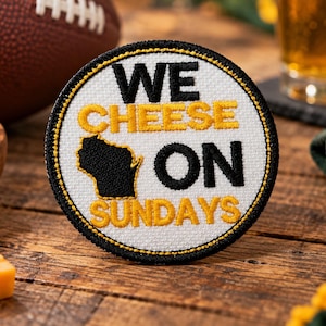 May include: A circular embroidered patch with a white background and a black border. The text reads WE CHEESE ON SUNDAYS in black and yellow thread. A black silhouette of the state of Wisconsin is positioned between the words CHEESE and ON.