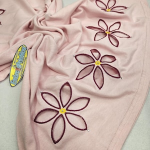 May include: A light pink fabric with embroidered flower designs. Each flower has a dark red outline, a yellow center, and small silver embellishments. The fabric is soft and appears to be a t-shirt or similar garment.