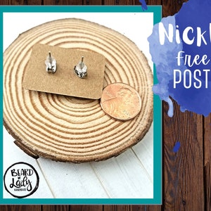 May include: A pair of silver stud earrings on a brown wooden surface with a penny for scale. The earrings are nickel free and the text "Beard Lady Handmade" is visible in the lower left corner.