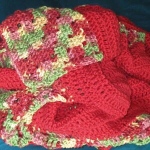 Puede incluir: Una manta de ganchillo hecha a mano en tonos de rojo, verde, rosa y amarillo. La manta presenta un patr&oacute;n de puntadas texturizadas y est&aacute; doblada, mostrando las diferentes secciones de color. El tema general es acogedor y hecho a mano.