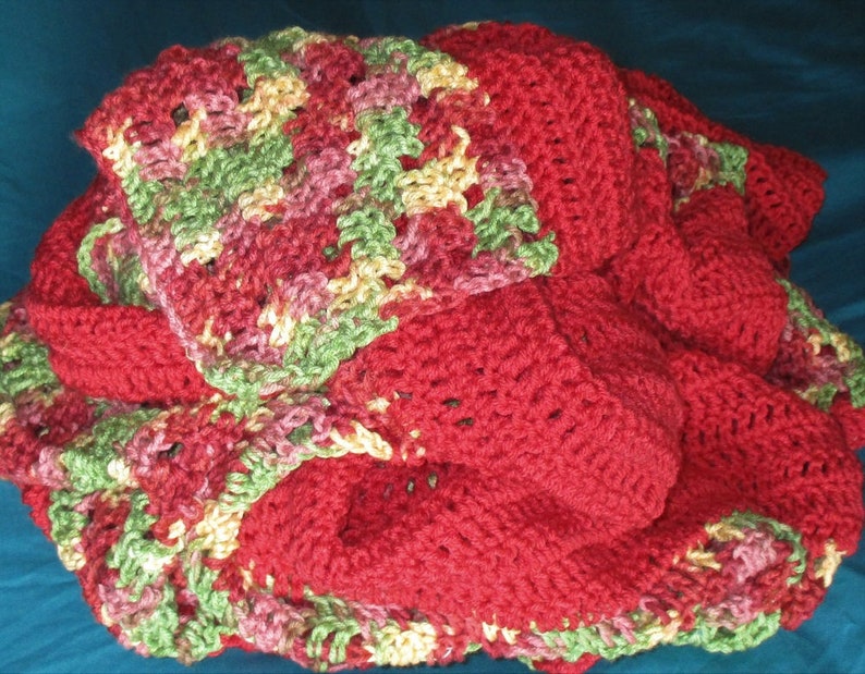 Puede incluir: Una manta de ganchillo hecha a mano en tonos de rojo, verde, rosa y amarillo. La manta presenta un patr&oacute;n de puntadas texturizadas y est&aacute; doblada, mostrando las diferentes secciones de color. El tema general es acogedor y hecho a mano.