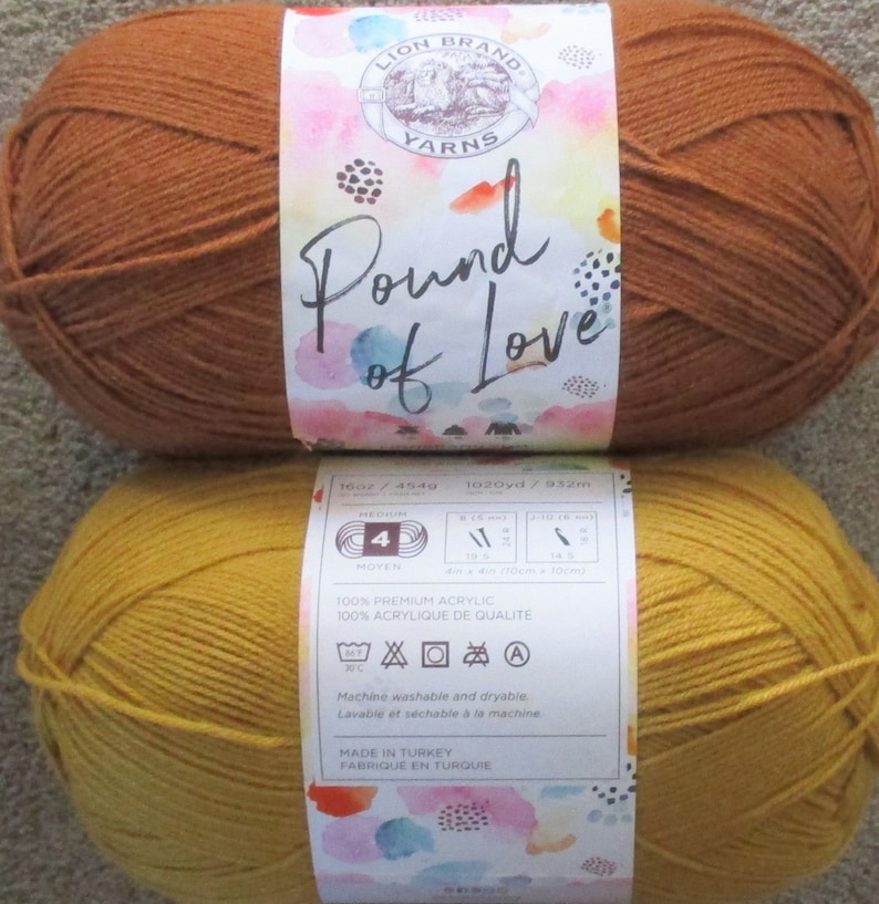 Może przedstawiać: Dwa motki wł&oacute;czki Lion Brand Pound of Love. Jeden motek jest w kolorze intensywnego pomarańczowego, a drugi w jasnym ż&oacute;łtym. Etykieta zawiera informacje: 100% Akryl Premium, 16 oz/454g, 1020yd/932m, Pranie w pralce i suszenie w suszarce.