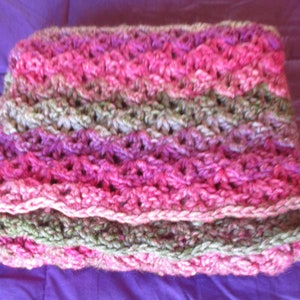May include: A crocheted scarf in shades of pink, green, and white. The scarf is made with a simple stitch pattern and has a soft, textured feel.