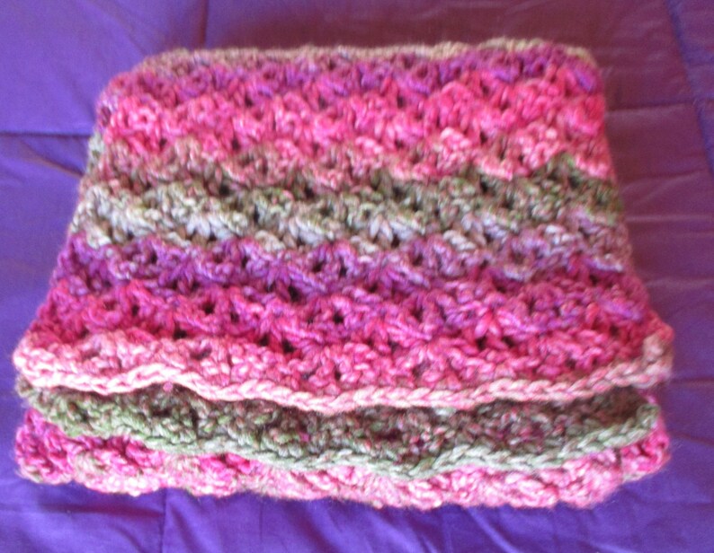 May include: A crocheted scarf in shades of pink, green, and white. The scarf is made with a simple stitch pattern and has a soft, textured feel.