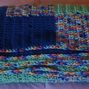 May include: A multi-colored crocheted blanket with blue, green, brown, and red stripes. The blanket is made of a soft, textured yarn and has a fringed edge.