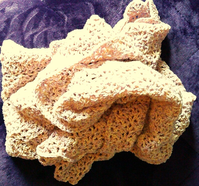 Pode incluir: Uma manta de croch&ecirc; feita &agrave; m&atilde;o, de cor creme. A manta &eacute; dobrada e em camadas, mostrando o intrincado padr&atilde;o de tecido aberto. O fio tem uma cor sutilmente variegada, com tons de castanho e bege. A manta &eacute; macia e texturizada.
