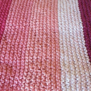 May include: A close-up of a knitted fabric with stripes of pink, red, white, and purple.