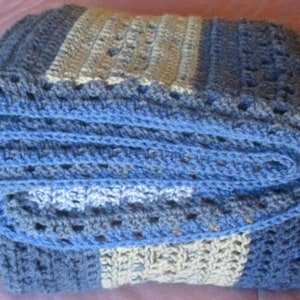 May include: A crocheted blanket in shades of blue and white. The blanket is folded in thirds and has a striped pattern.