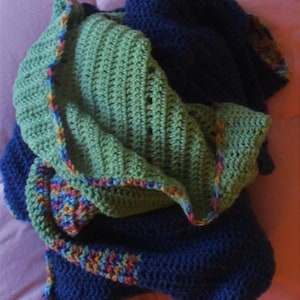 May include: A green and blue crocheted blanket with a colorful border. The blanket is folded in half and has a soft, textured appearance.