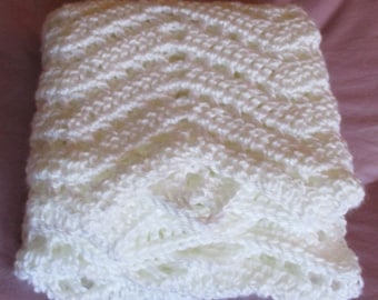 May include: A white crocheted baby blanket with a lacy pattern. The blanket is folded in half and is lying on a pink surface.