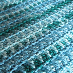 May include: A close-up of a blue and teal crocheted blanket with a textured pattern.