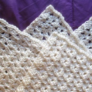 May include: A white crocheted shawl with a delicate, lacy pattern. The shawl is made of fine yarn and has a soft, airy feel.