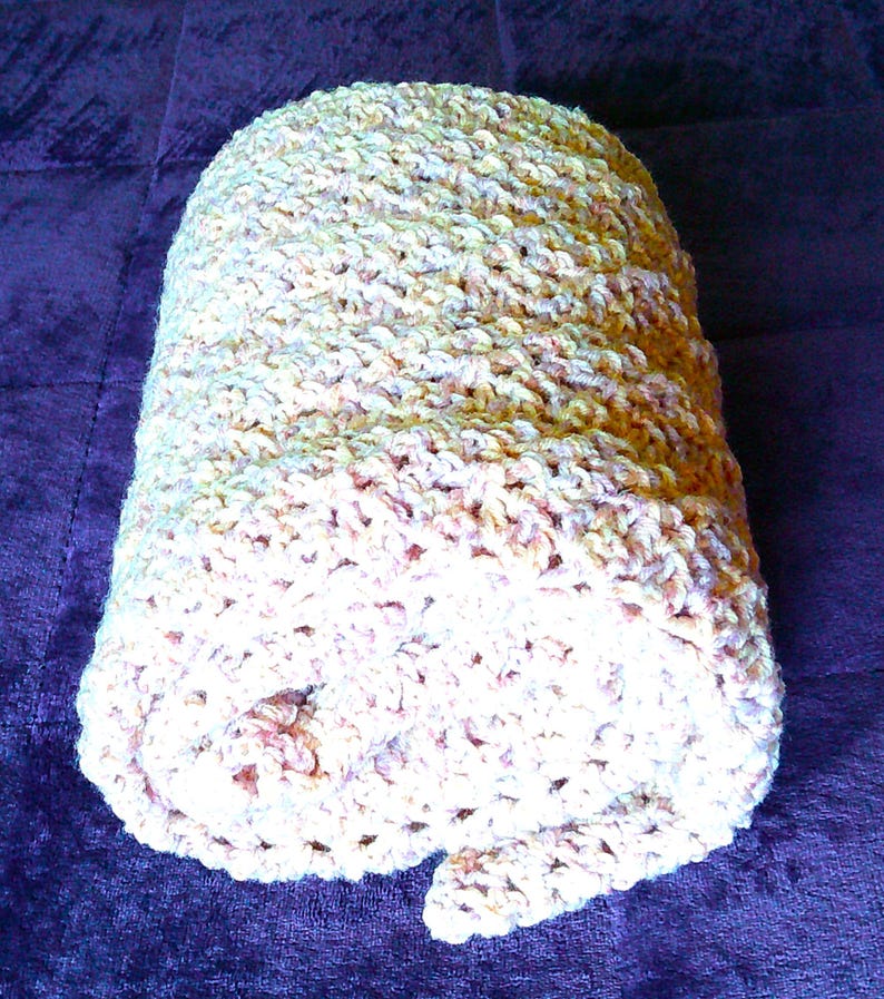 Pode incluir: Um cobertor enrolado, feito &agrave; m&atilde;o, em tons de creme, bege e p&ecirc;ssego. O cobertor tem uma apar&ecirc;ncia espessa e texturizada, sugerindo uma constru&ccedil;&atilde;o de croch&ecirc; ou tric&ocirc;. As cores suaves evocam calor e conforto.