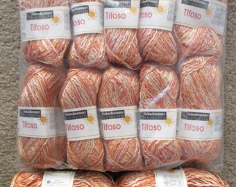 May include: A close-up of 10 balls of orange and white yarn with the label "Schachenmayr nomotta Tifoso" on each ball. The yarn is packaged in a clear plastic bag.