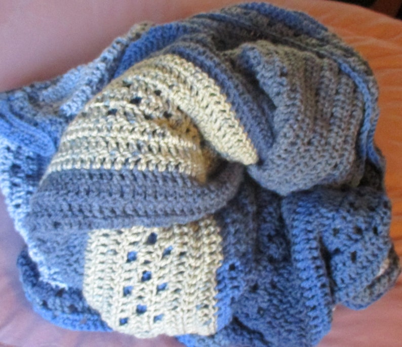 May include: A blue and white crocheted blanket with a textured pattern. The blanket is folded and appears soft and cozy.