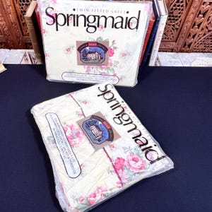 May include: Two packages of Twin Fitted Sheets by Springmaid. The sheets are cream-colored with a floral pattern in pink and green. The packaging includes the text "Springmaid" and "Twin Fitted Sheet."
