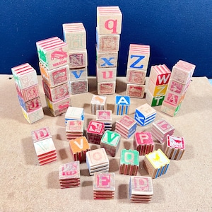 May include: A collection of vintage wooden alphabet blocks in various colors. The blocks feature letters, numbers, and small illustrations. Some blocks are stacked, while others are scattered, creating a playful arrangement. The blocks have a distressed, antique appearance.
