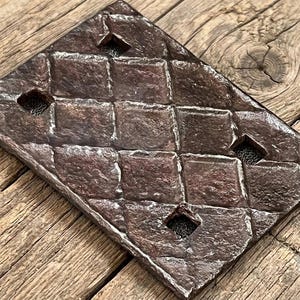 May include: A rectangular dark brown metal wall plate featuring a raised diamond grid pattern. The plate has four square cutouts positioned at the corners of the central diamond shapes, revealing a dark mesh screen underneath the metal surface.
