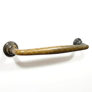 May include: An antique brass-toned cabinet pull handle. The handle is curved with decorative circular end pieces. The brass finish has a mottled appearance, suggesting age and use. The handle is designed for easy gripping and pulling.