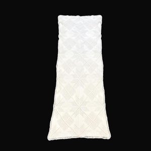 May include: A white, rectangular table runner with a detailed, geometric pattern. The runner is made of a textured fabric and has a delicate, scalloped edge. The design features repeating star-like shapes.