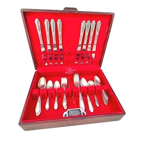 May include: A wooden silverware case with a red velvet interior, showcasing a complete set of silver utensils. The set includes forks, spoons, and knives, neatly arranged. The case is open, revealing the contents, and is set against a white background.