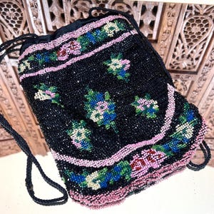 May include: Black beaded drawstring bag with floral embroidery in pink, blue, and green. The bag features a pink beaded border and a black drawstring closure. The bag is likely vintage or antique.
