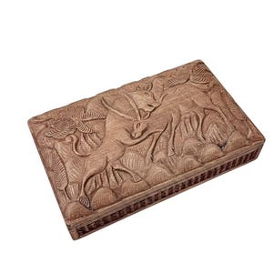 May include: A rectangular wooden box with a detailed carved relief depicting two deer in a forest setting. The box is a warm brown color and has a decorative border around the edges.