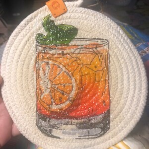 May include: A white rope coaster with a graphic of a glass of orange juice with a lime wedge and a sprig of mint.